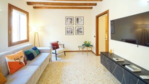 A living room with a sofa, a TV, and a small table with a plant. - DolceVita Apartments N. 519 (Venice)