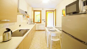 A compact kitchen with a microwave, kettle, and a refrigerator. There is a dining table with chairs and a window with a view of the outside. - DolceVita Apartments N. 519 (Venice)