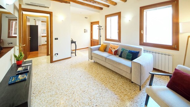 A spacious living area with a sofa, a coffee table, and a large window providing natural light. - DolceVita Apartments N. 519 (Venice)