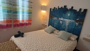 A bedroom with a bed, a bedside table, a chair, and a wall-mounted lamp.