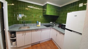 A kitchen with green tiles, a sink, a stove, and a refrigerator.