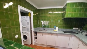 A compact kitchen with green tiled walls, a washing machine, a sink, and a countertop.