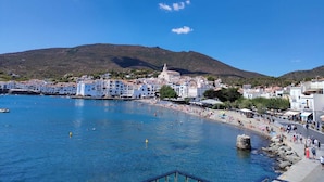 A coastal town with white buildings, a beach, and a mountain in the background.