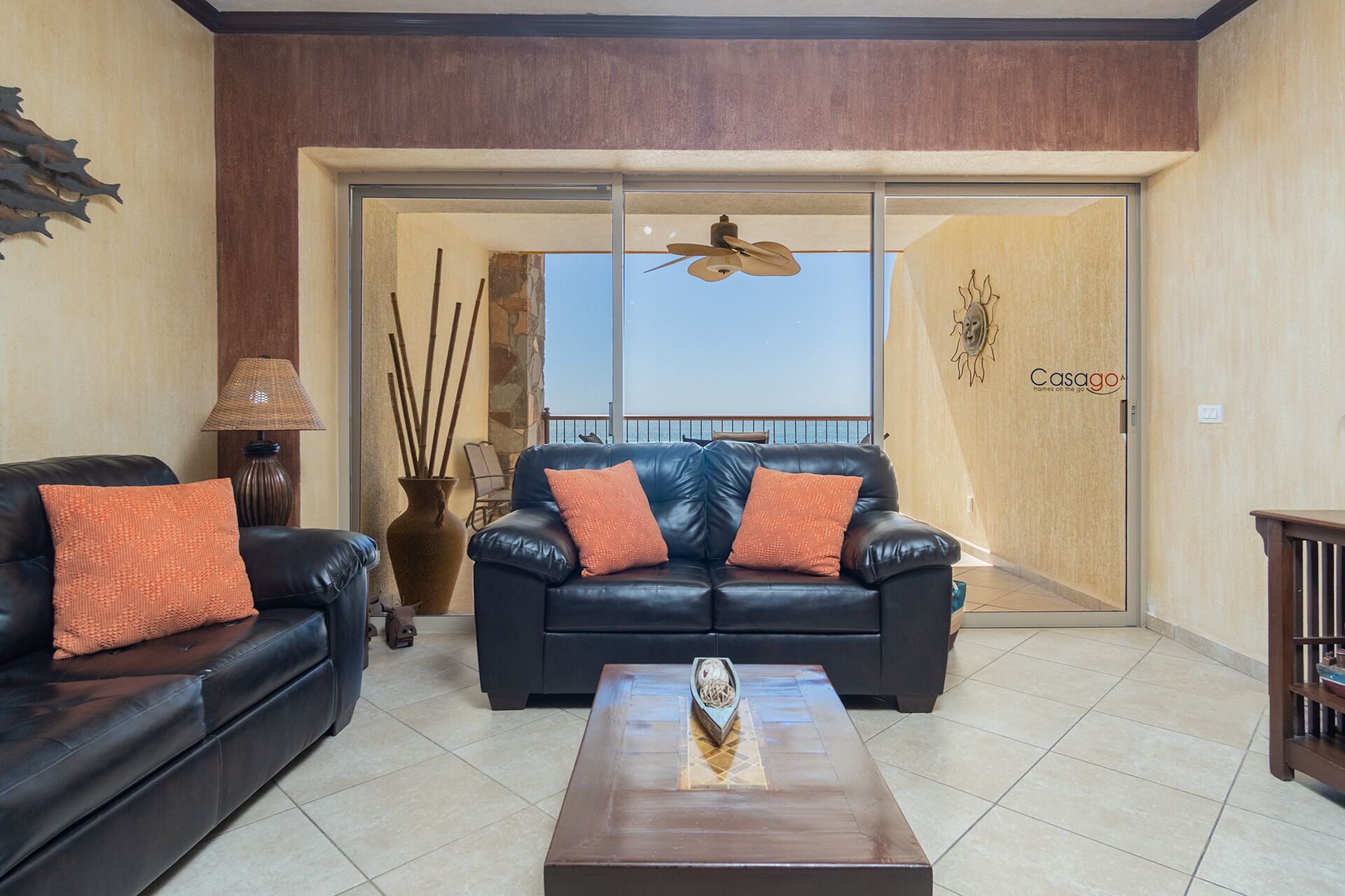 A living room with a black leather sofa, a coffee table, and a view of the sea through a sliding door.