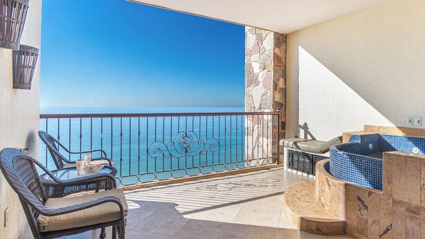 Een balkon met rieten meubilair, een stenen muur en uitzicht op zee.