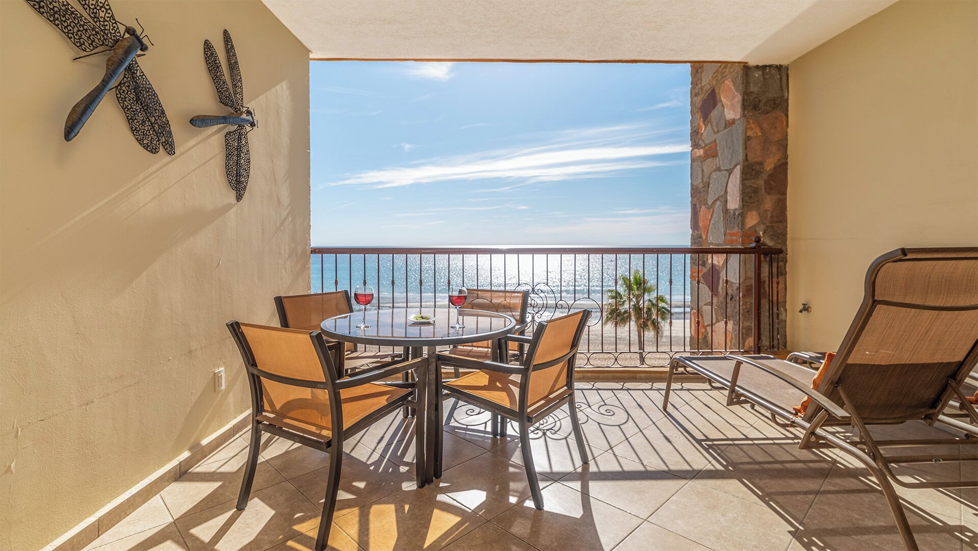 A balcony with a table and chairs, a view of the ocean, and decorative wall art.