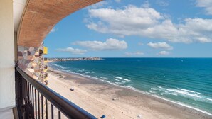 Uitzicht op het strand vanaf een balkon, met een stenen muur en een metalen hekwerk.