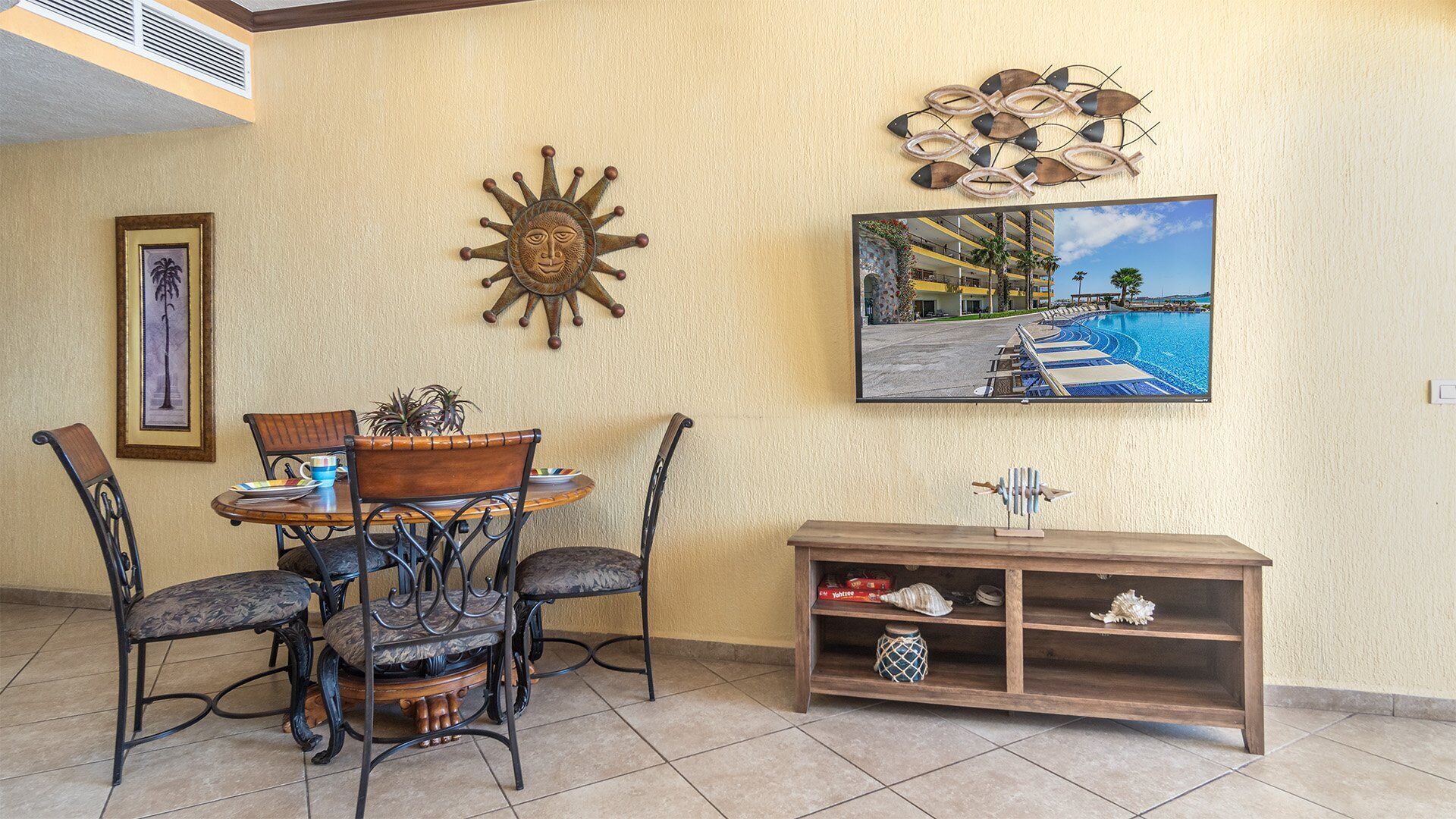 Un área de comedor con una mesa redonda y cuatro sillas, un adorno en la pared, un cuadro enmarco y una estantería con objetos decorativos.