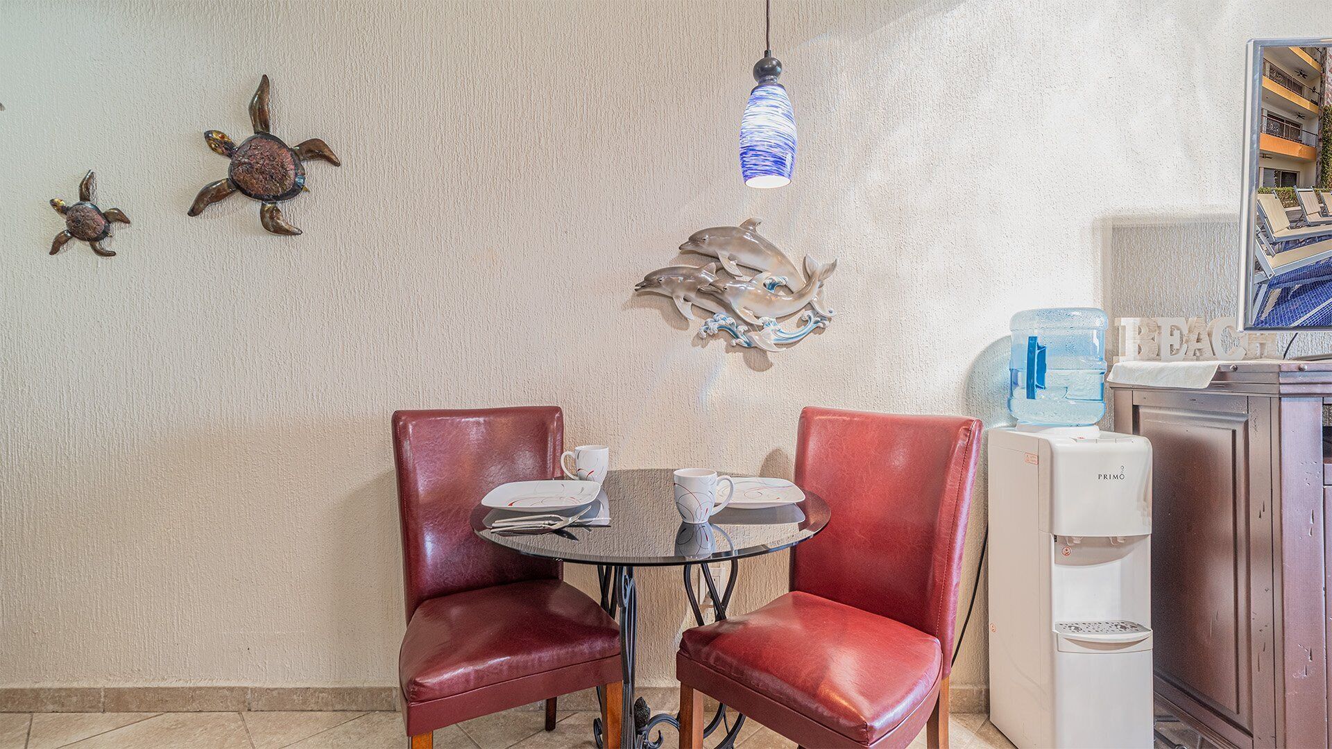 Comedor con una mesa redonda, dos sillas de cuero rojo y una pared decorada con detalles artísticos.