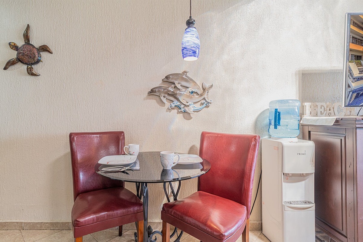Comedor con una mesa redonda, dos sillas de cuero rojo y una pared decorada con detalles artísticos.