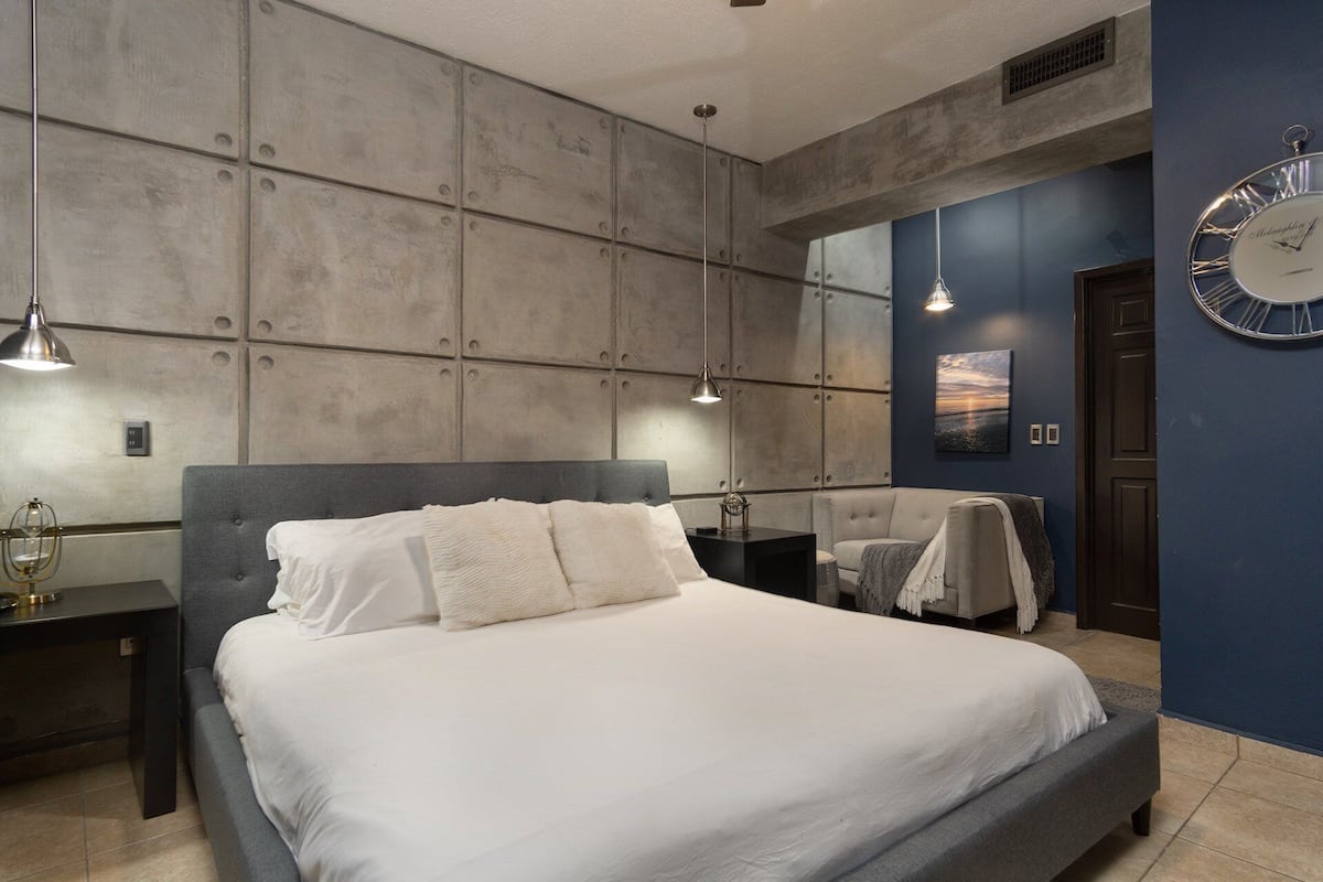A modern bedroom with a large bed, two bedside tables, a wall clock, and a painting.