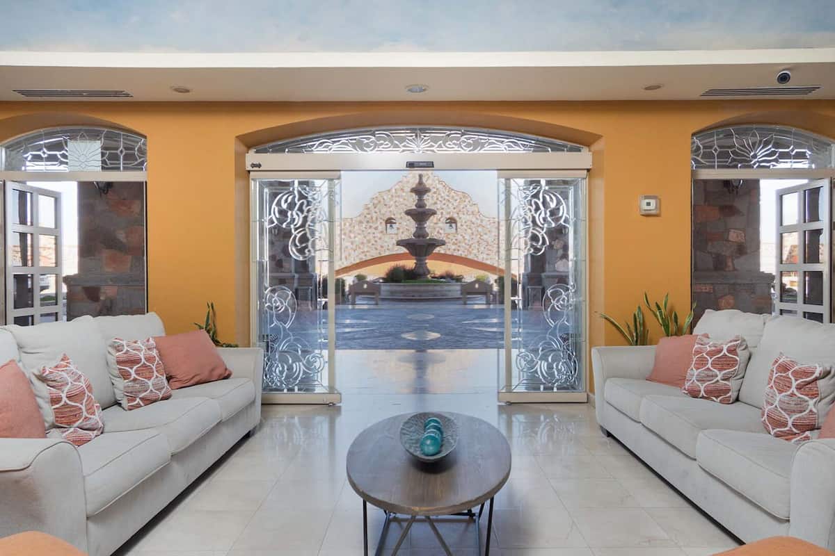 Un hall d’entrée avec deux canapés, une table basse et une vue sur une fontaine, visible à travers une porte vitrée.