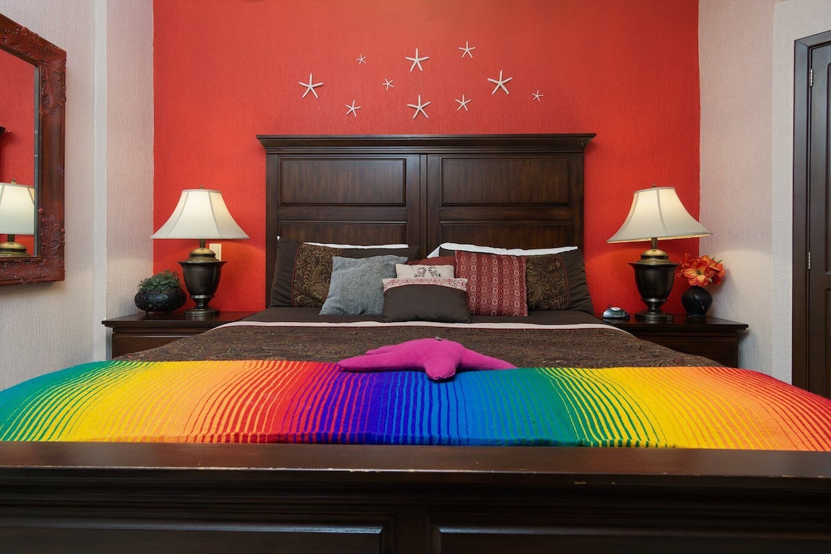 A hotel room with a large bed, two bedside tables with lamps, a red wall with star decorations, and a wooden headboard.