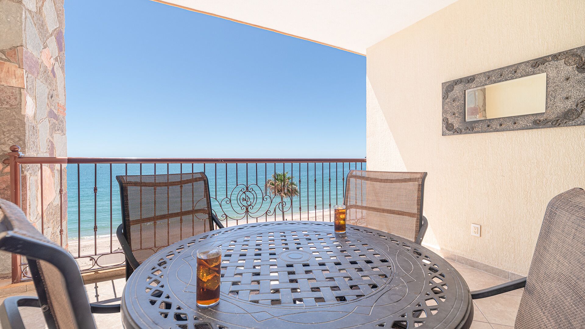 A balcony with a table and chairs, overlooking a beach.
