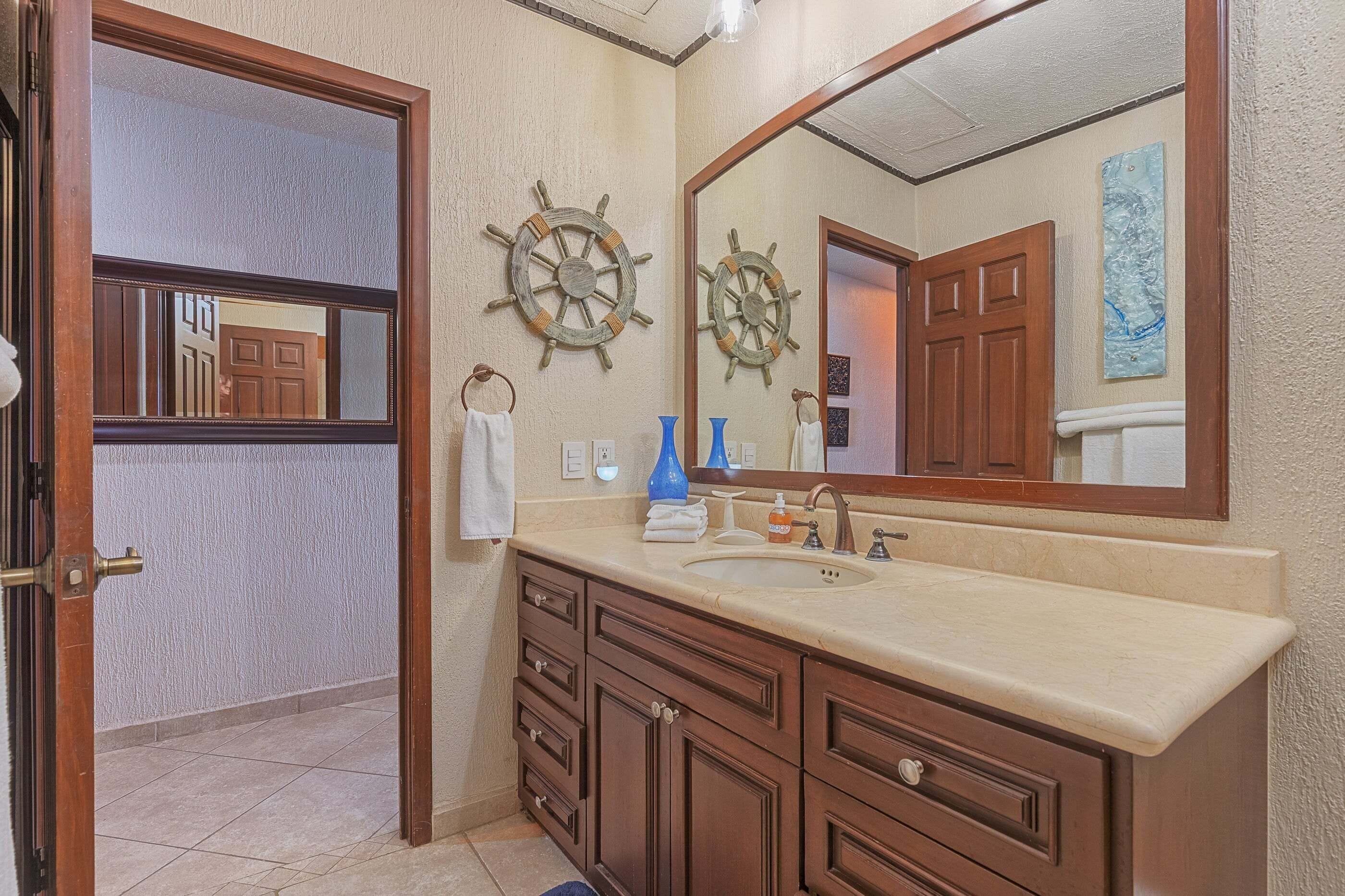 A bathroom with a large mirror, wooden vanity, and two ship wheel decorations.