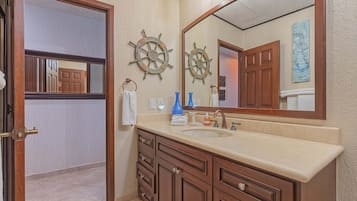 A bathroom with a large mirror, wooden vanity, and two ship wheel decorations.