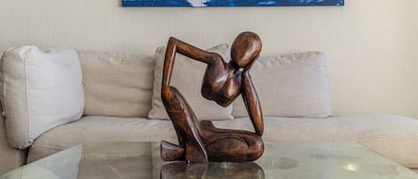 Une sculpture est posée sur une table en verre devant un canapé beige. Au mur, on peut voir un tableau abstrait bleu.