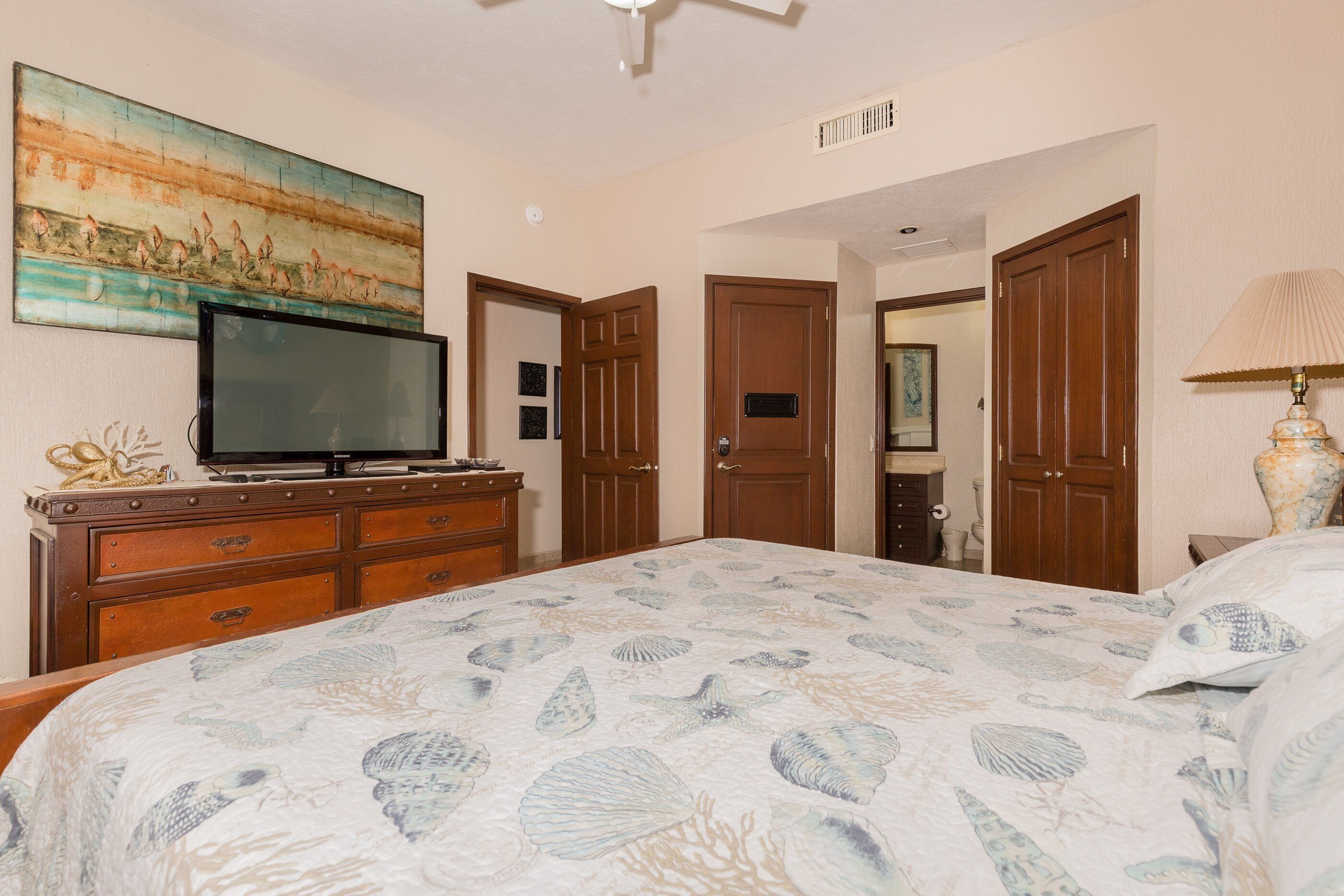 A hotel room with a bed, a television on a dresser, and a painting on the wall.