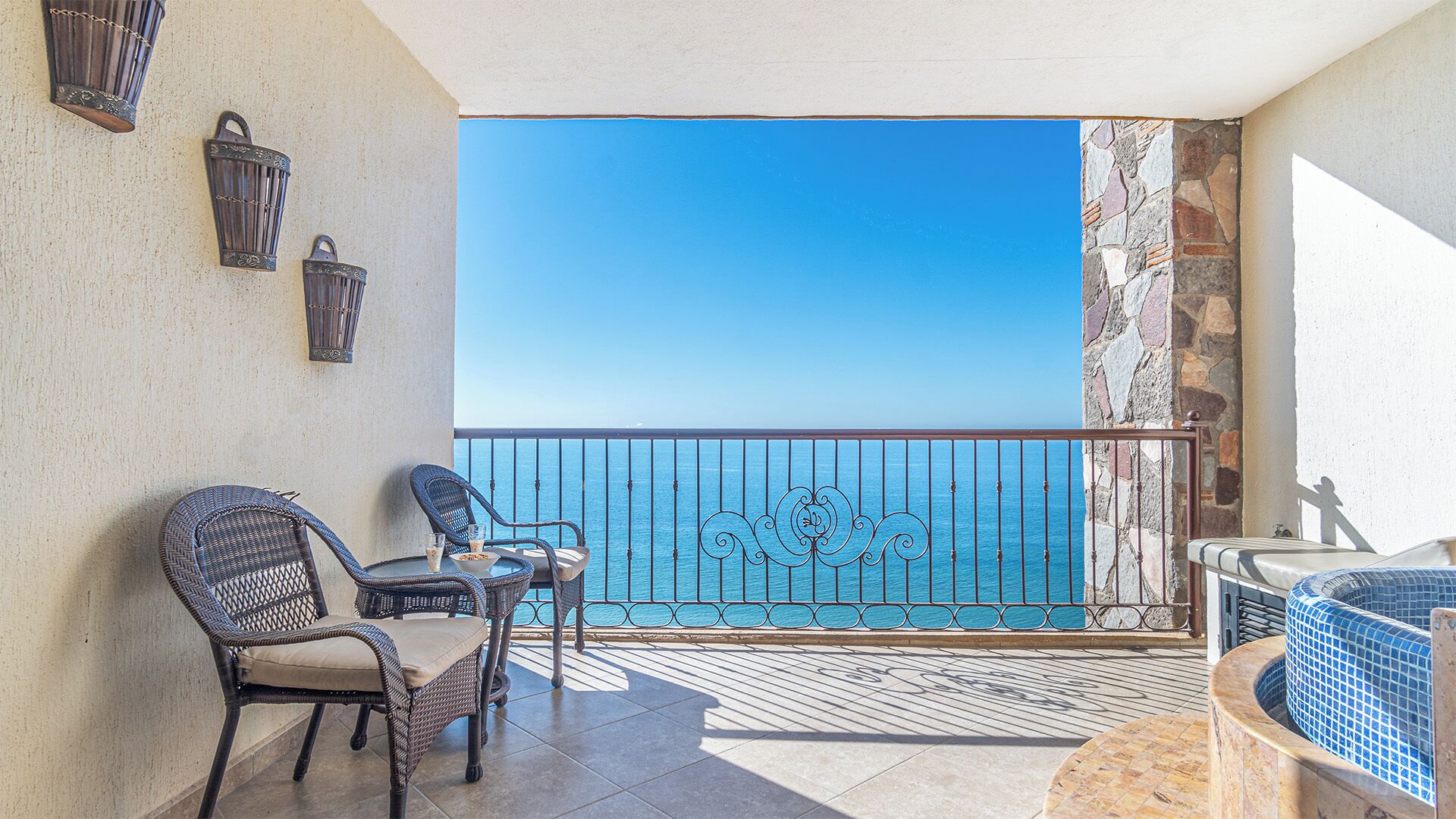 Un balcon avec des fauteuils en osier, une petite table et une vue sur la mer.