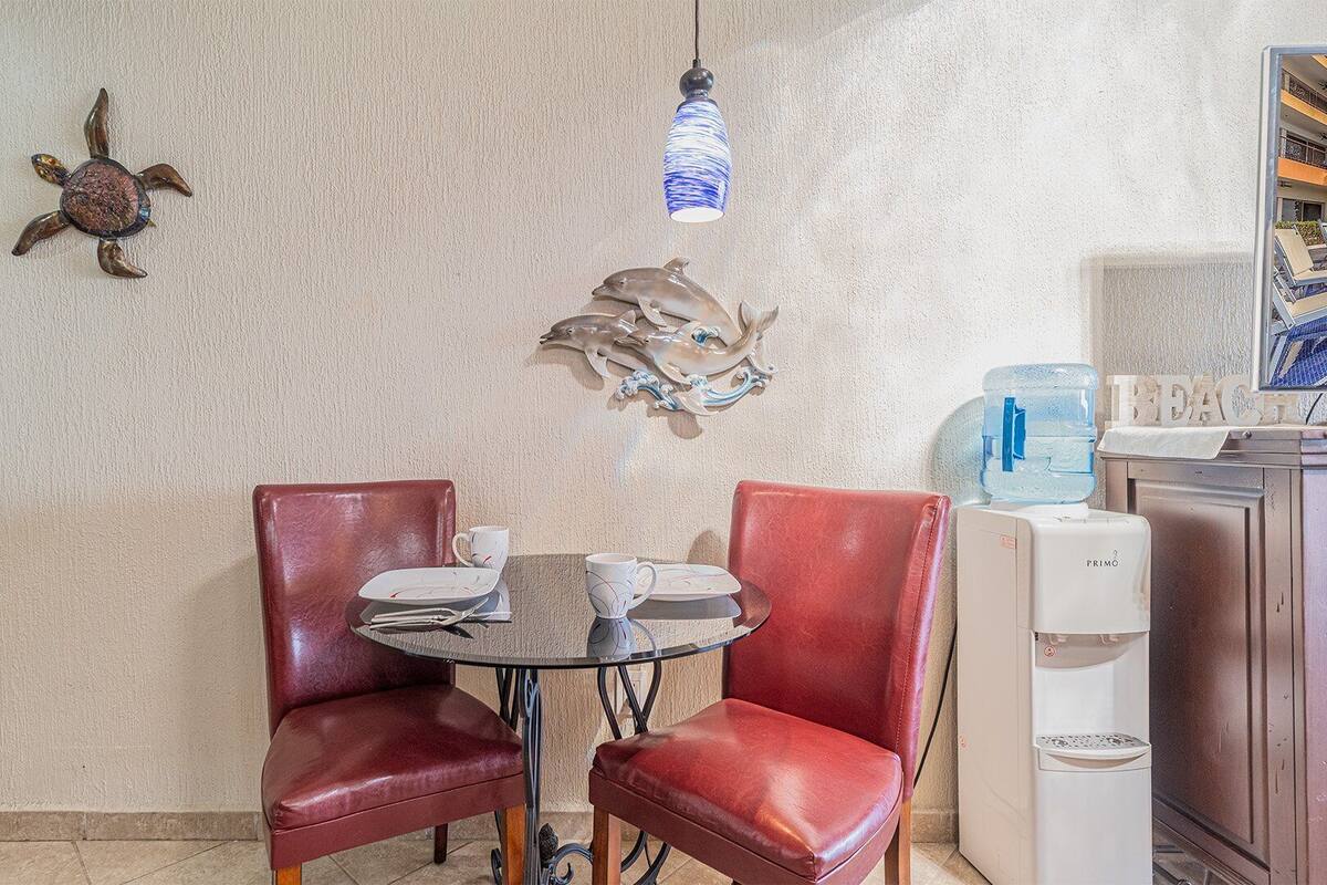 Un coin repas comprenant une table ronde, deux fauteuils en cuir rouge et un mur agrémenté d’œuvres d’art décoratives.