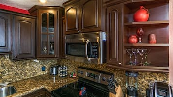 A kitchen with dark wooden cabinets, a granite countertop, a stainless steel stove, a microwave, a blender, and a coffee maker.