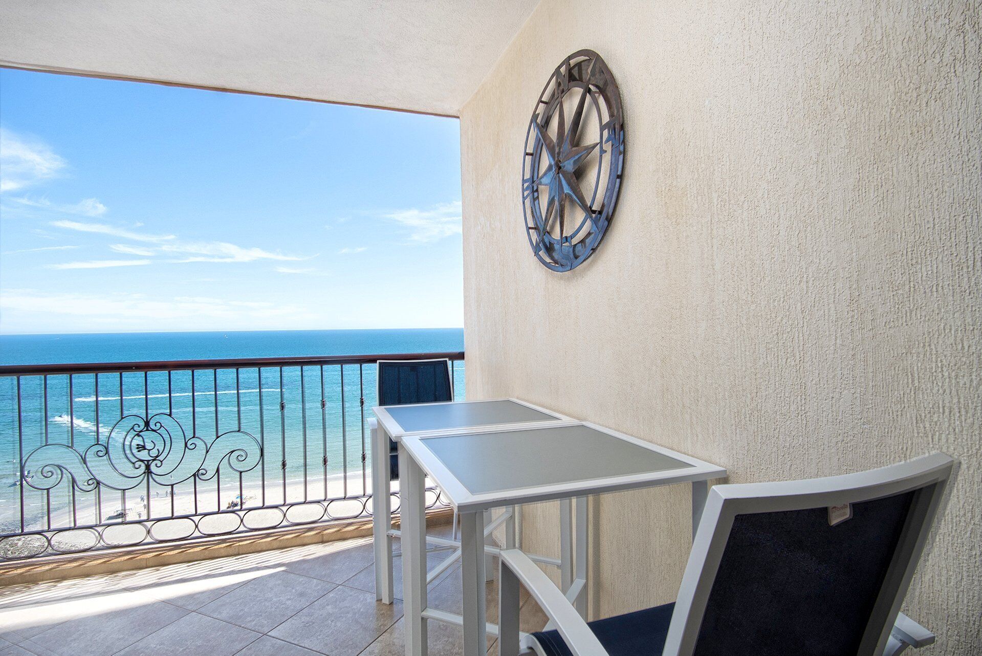 Un balcón con mesa y silla, un adorno metálico en la pared, y vista al océano.