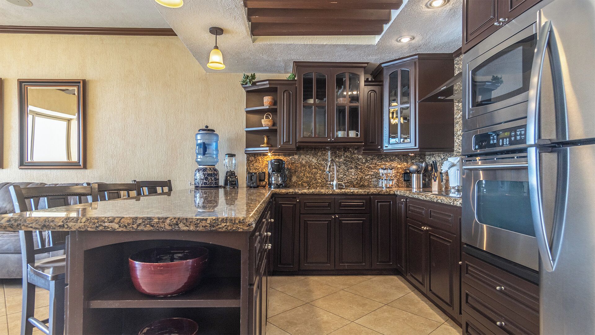 A kitchen with dark wooden cabinets, a stainless steel refrigerator, granite countertops, and a built-in oven.