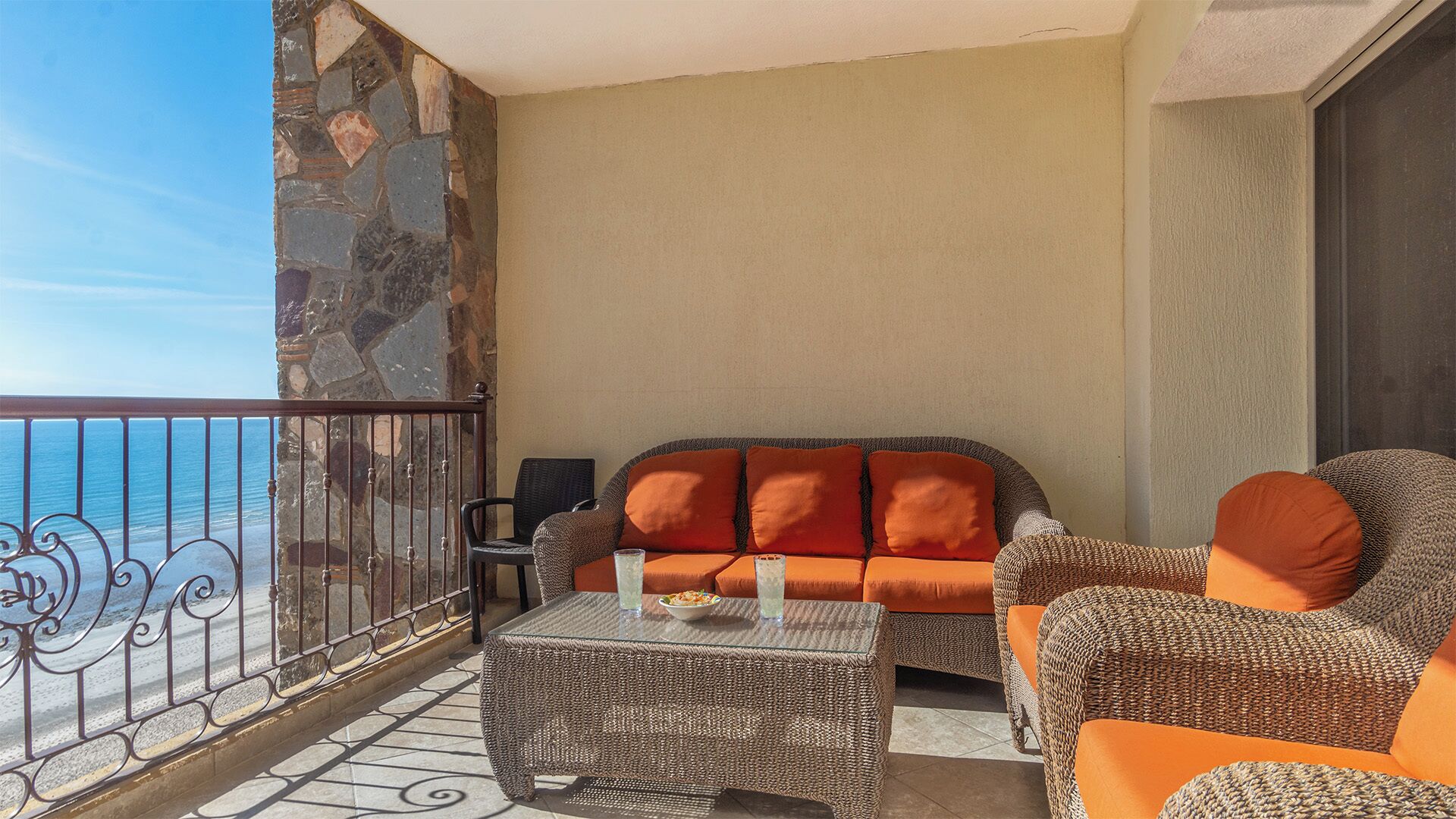 Un balcón con pared de piedra, muebles de mimbre y vista al mar.