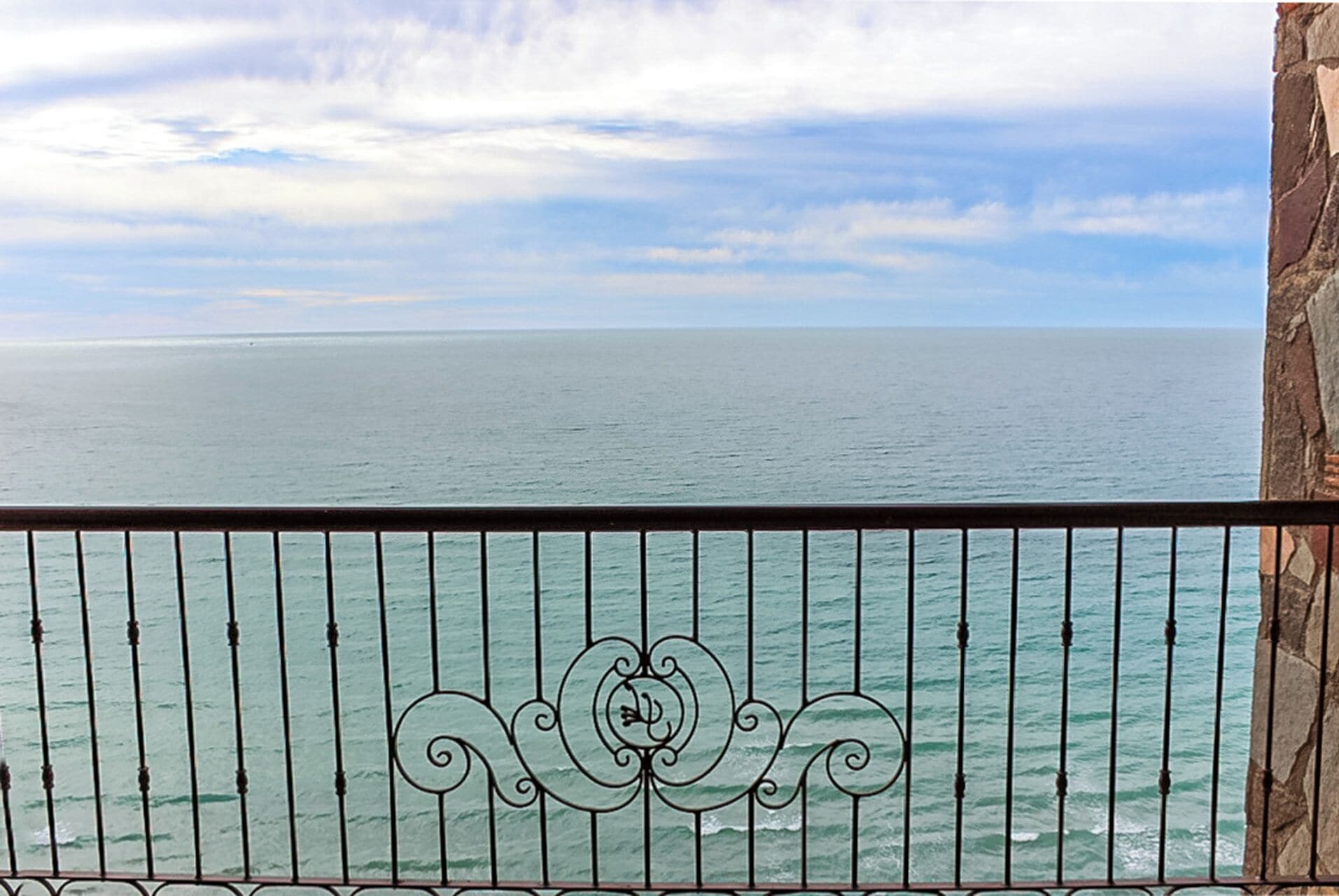 A balcony with a metal railing overlooking a calm sea.