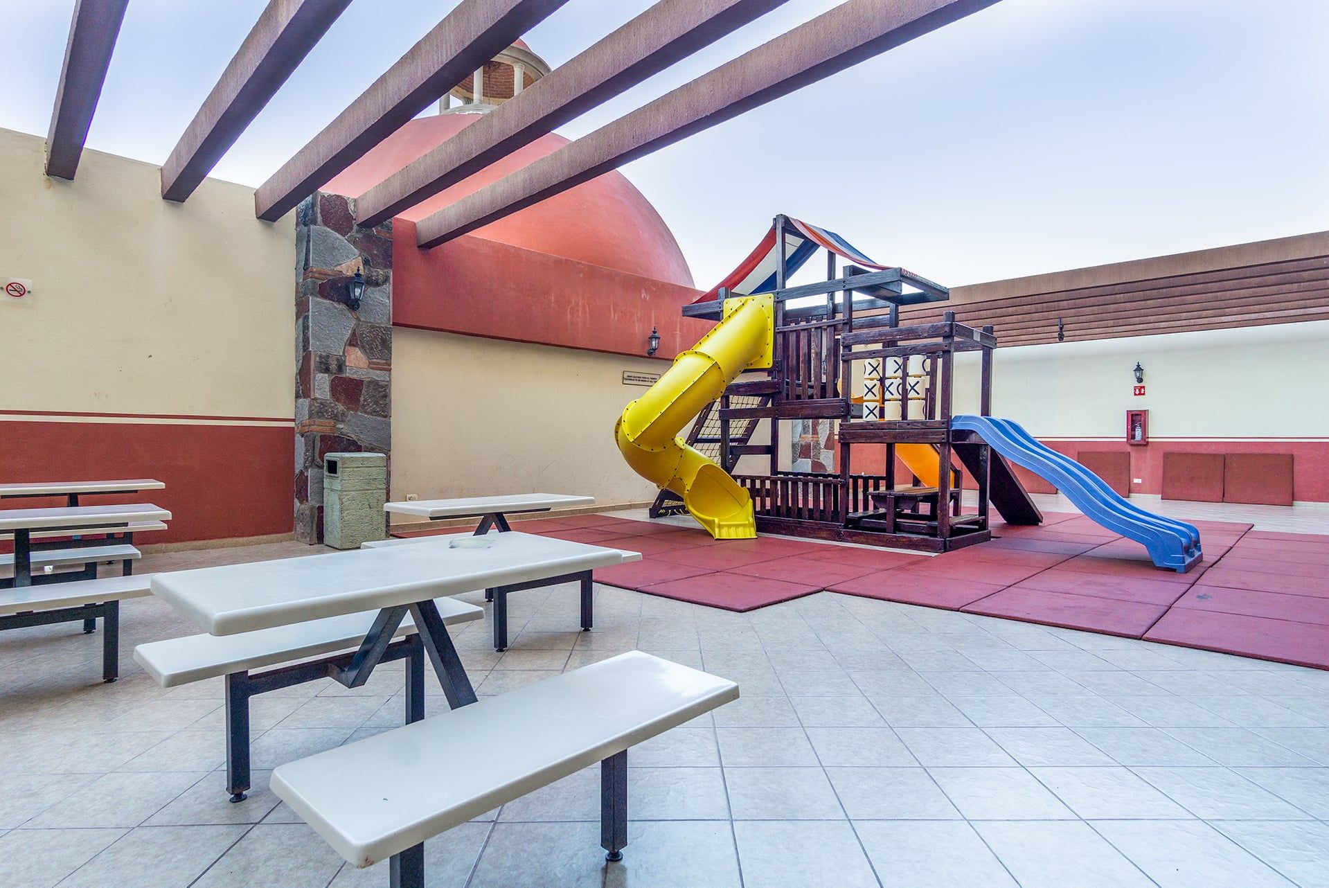 Ein Spielplatz im Freien mit Rutsche, Picknicktischen und einer Kletterkonstruktion.