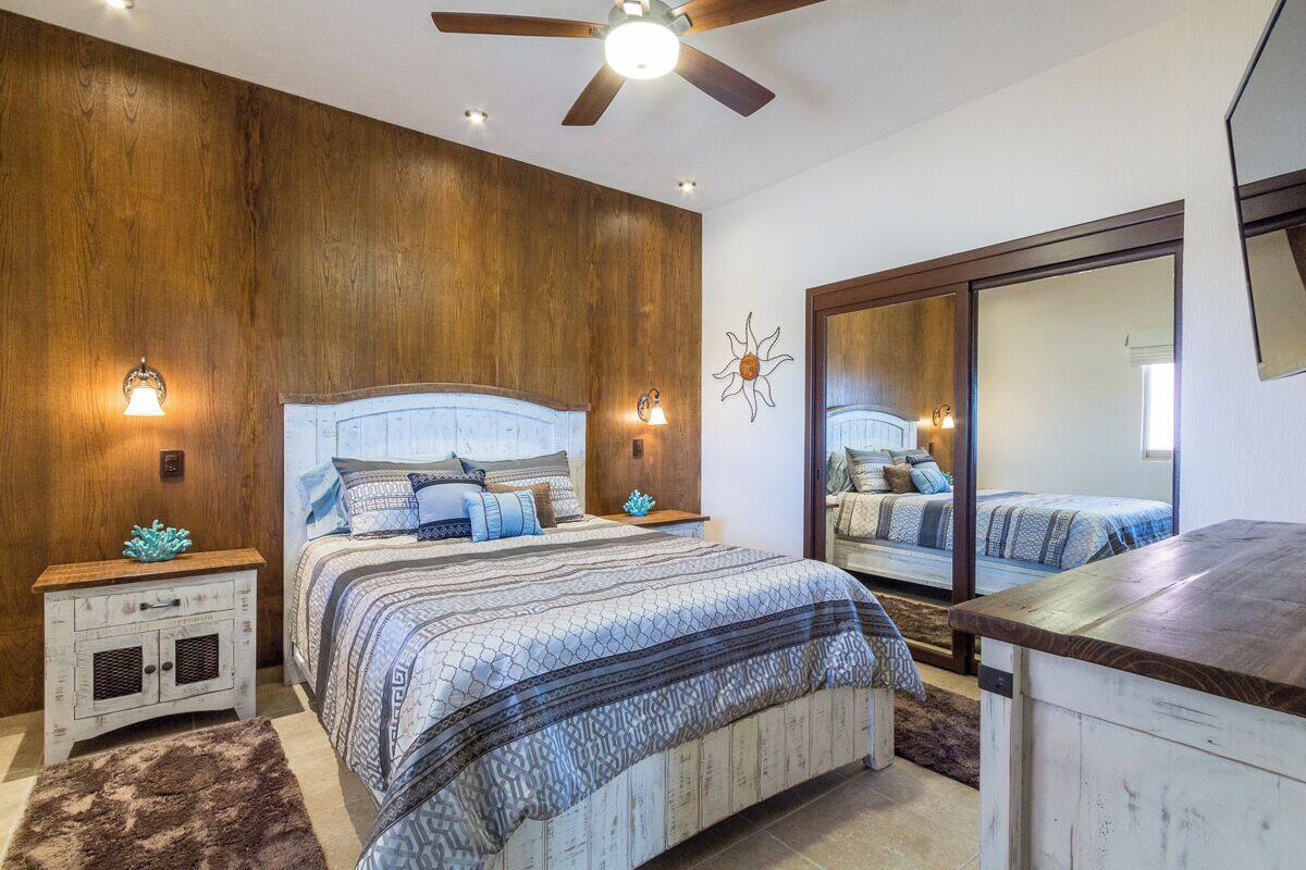 Une chambre avec un grand lit, des murs en bois, un ventilateur de plafond et un miroir.