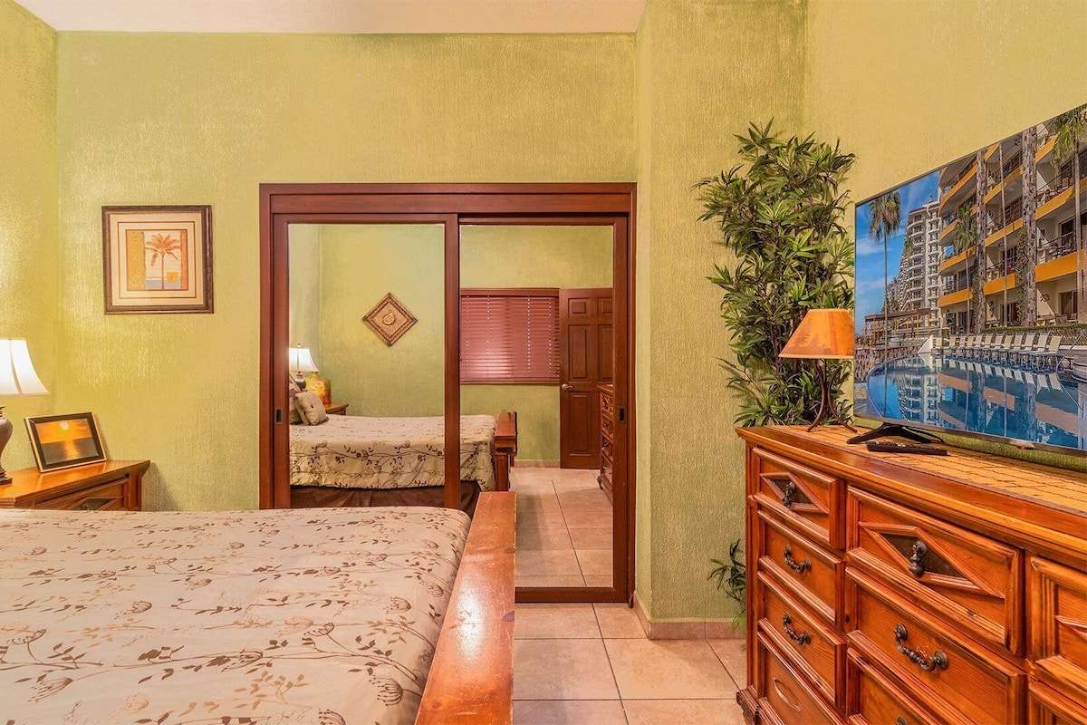 Une chambre d’hôtel comprenant un lit, une table de chevet, une commode, un miroir et une porte donnant sur une autre pièce.