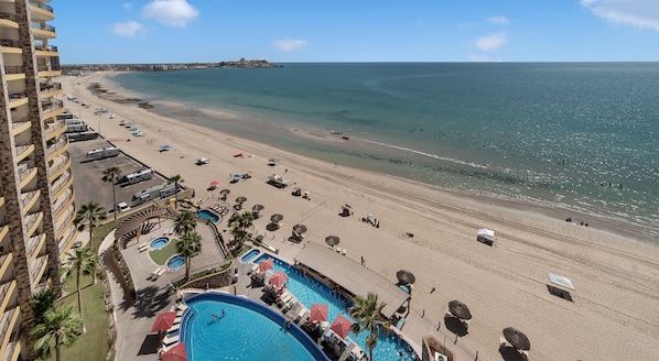 A beach resort with a swimming pool, beach umbrellas, and a view of the ocean. - Sonoran Sky II (Puerto Peñasco)