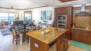 Un amplio salón con mesa de comedor, una cocina con encimeras de granito y vistas al océano.