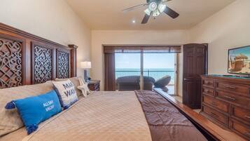 A bedroom with a bed, a dresser, a television, and a view of the ocean through a sliding door.
