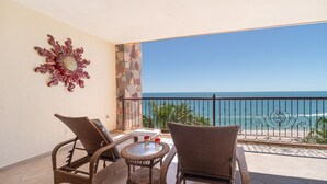 A balcony with wicker furniture, a decorative wall piece, and a view of the ocean.