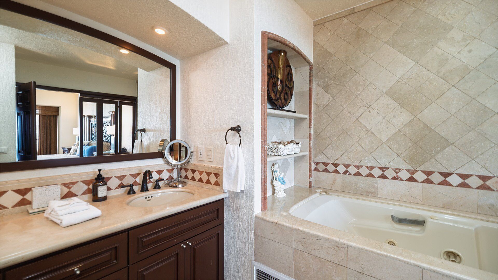 Un baño con un espejo grande, un lavabo con tocador, una bañera y un estante decorativo.