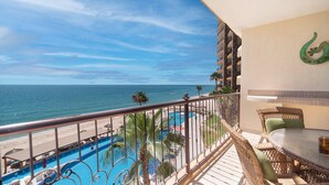 A balcony with a view of the ocean, a pool, and outdoor furniture.