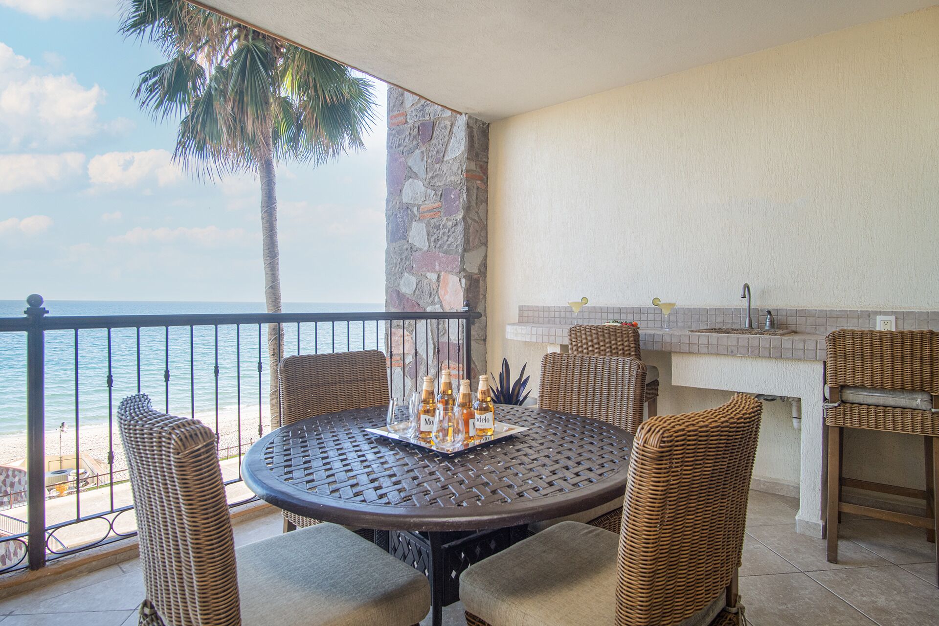 A balcony with a round table, wicker chairs, a small bar area, and a view of the ocean.