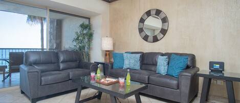 A living room with two grey sofas, a glass coffee table, and a round mirror on the wall.