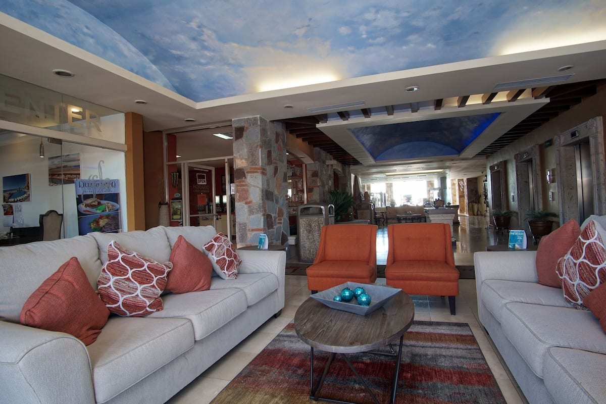 Een ruime lobby met een modern ontwerp, voorzien van een grote zithoek met banken en fauteuils, een centrale salontafel en een plafond met een wolkenfries.