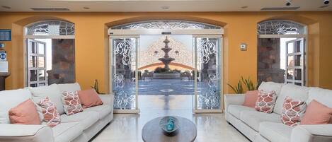 Eine geräumige Lobby mit zwei Sofas, einem Couchtisch und Blick auf einen Brunnen durch dekorative Glasscheiben.