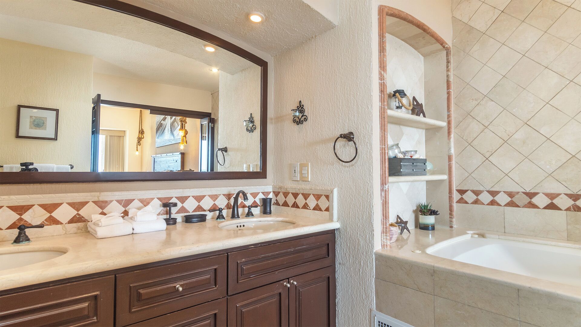 A bathroom with two sinks, a large mirror, a bathtub, and decorative wall tiles.