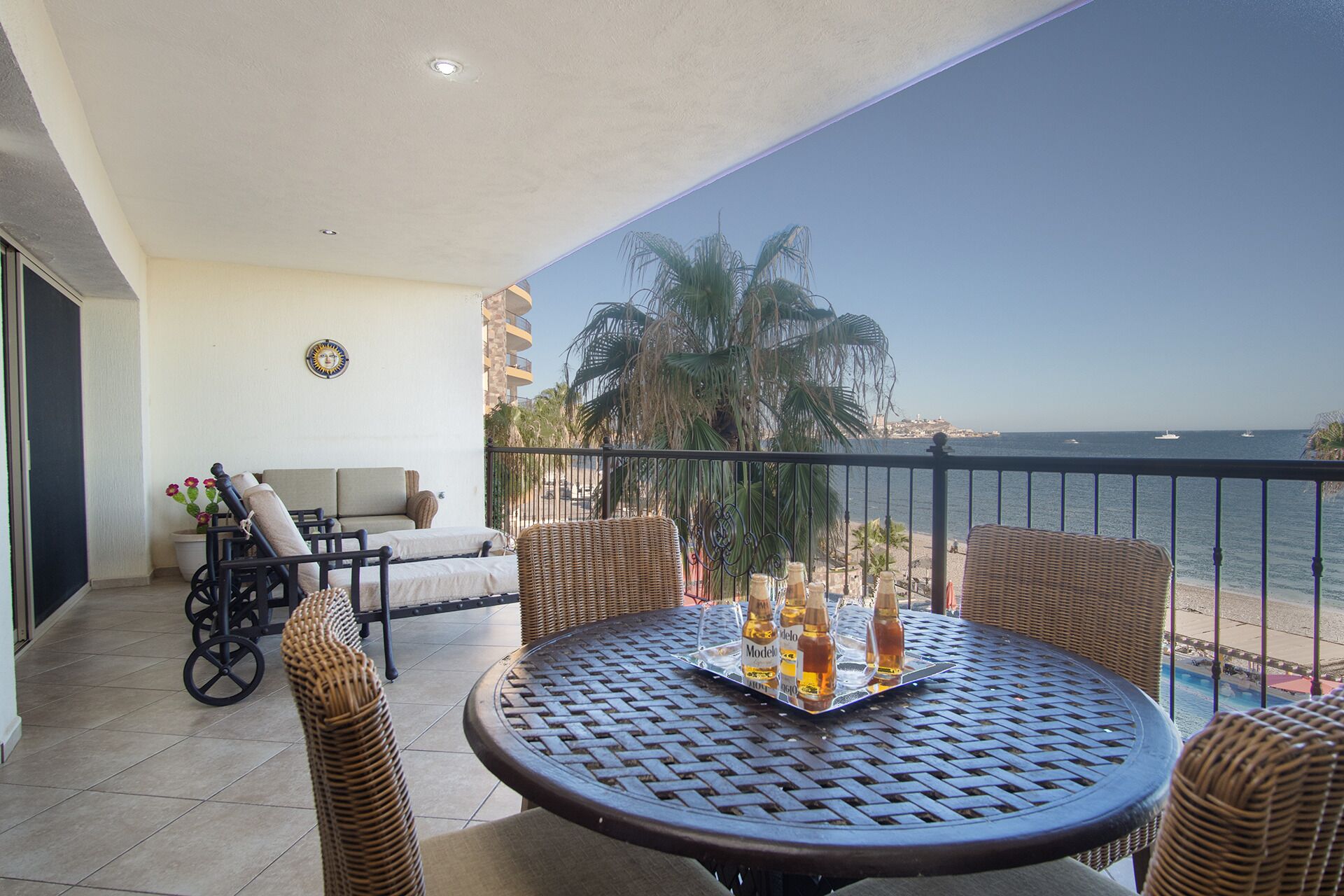 A balcony with wicker furniture, a table with bottles, and a view of the sea.