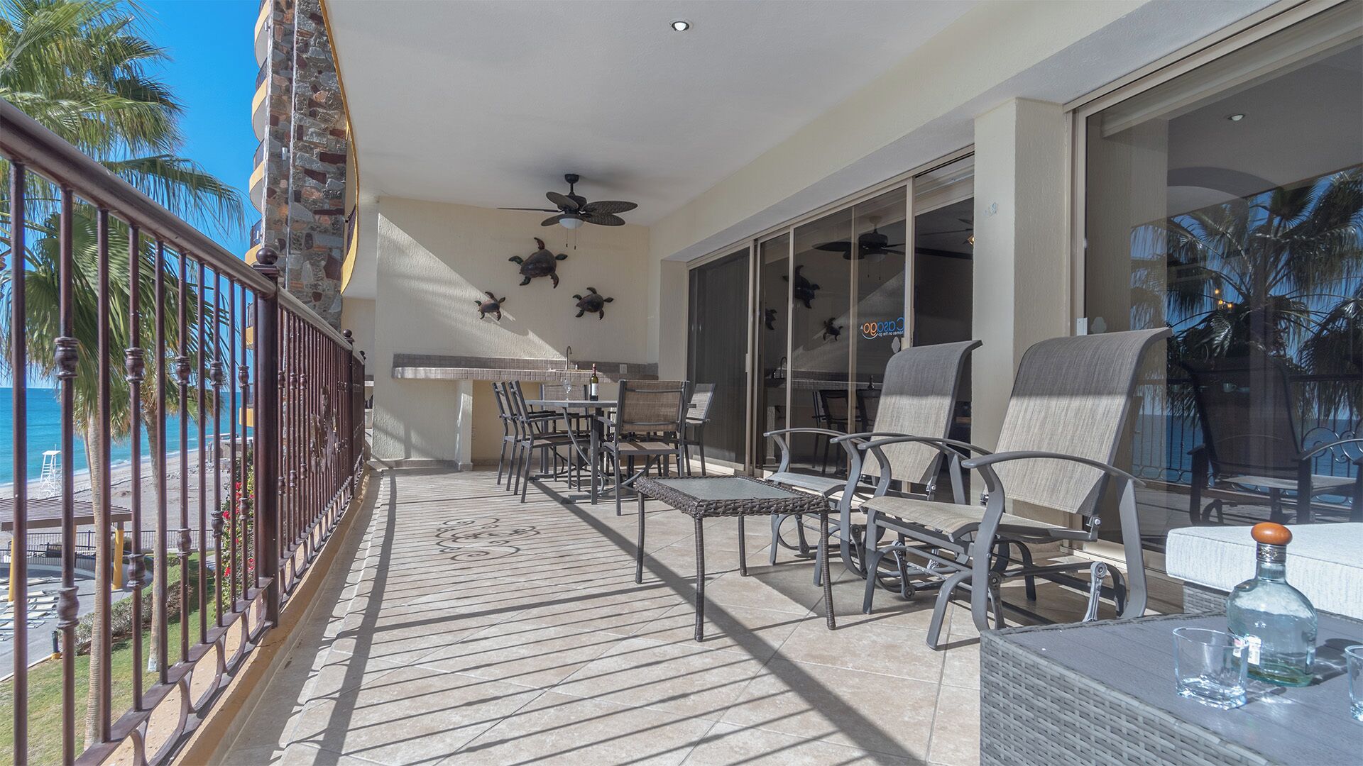A balcony with a view of the ocean, furnished with chairs and a table, and a ceiling fan.