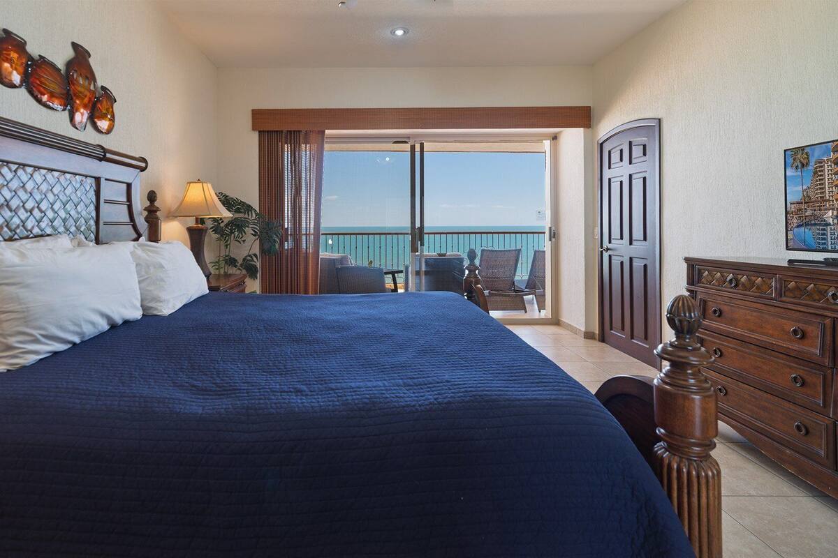 Een hotelkamer met een groot bed, een houten dressoir, een balkon met uitzicht en een televisie.