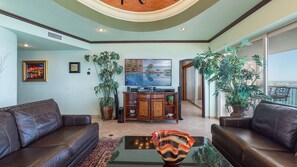 A living room with leather sofas, a glass coffee table, a TV, and a large potted plant.