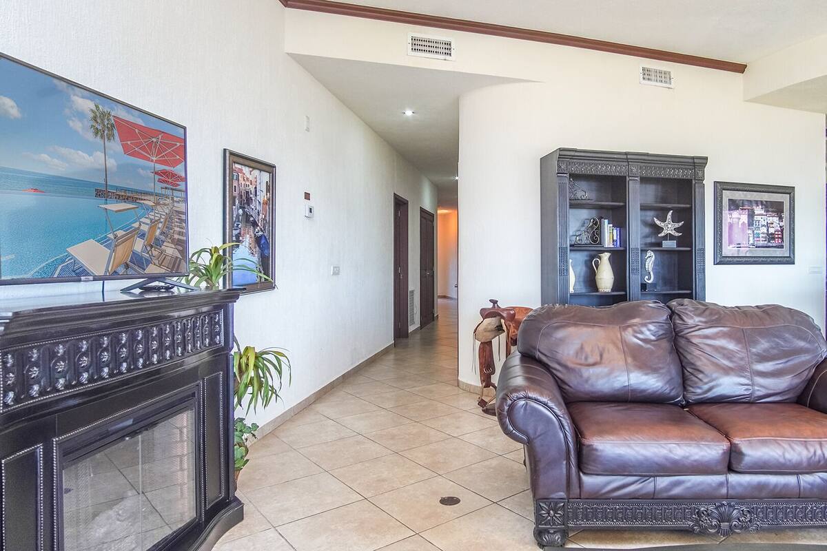 A spacious living room with a leather sofa, a fireplace, and a television displaying a beach scene.
