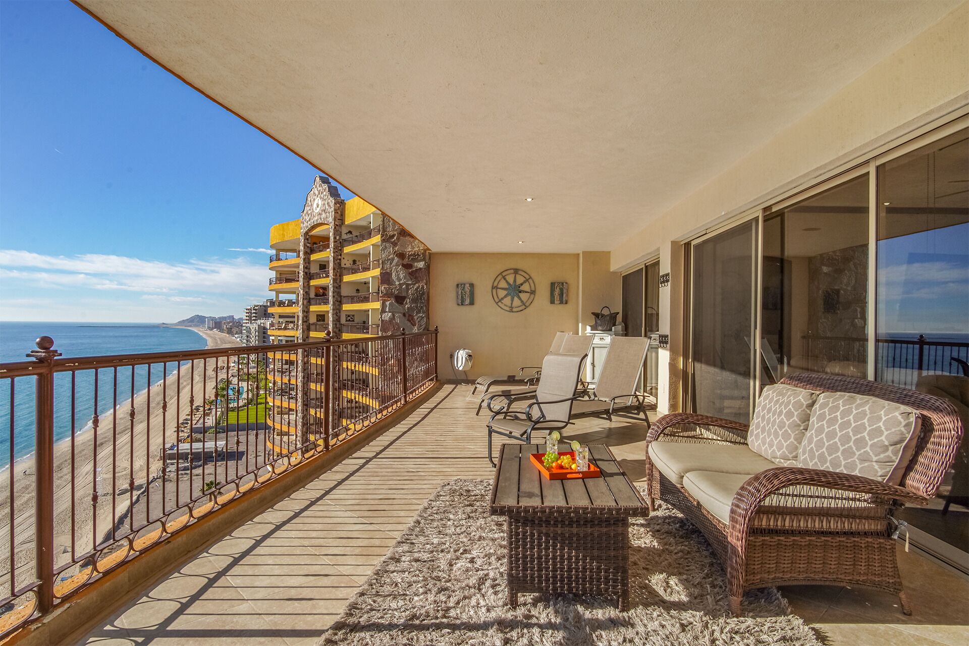 A balcony with a view of the beach, wicker furniture, and a star wall decoration.