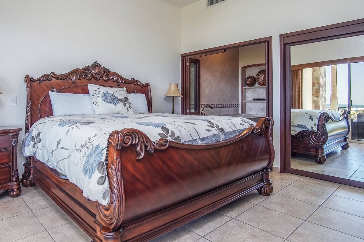 Une chambre à coucher avec un grand lit en bois, deux tables de chevet, une commode et un grand miroir.